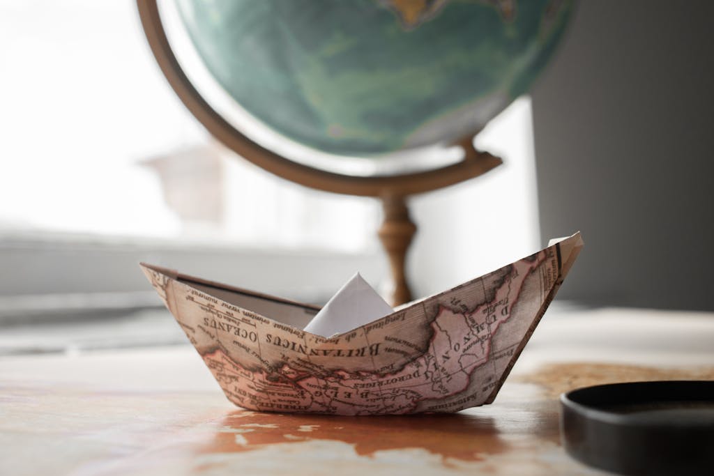 A paper boat crafted from a map sitting on a desk with a globe in the background, symbolizing exploration.